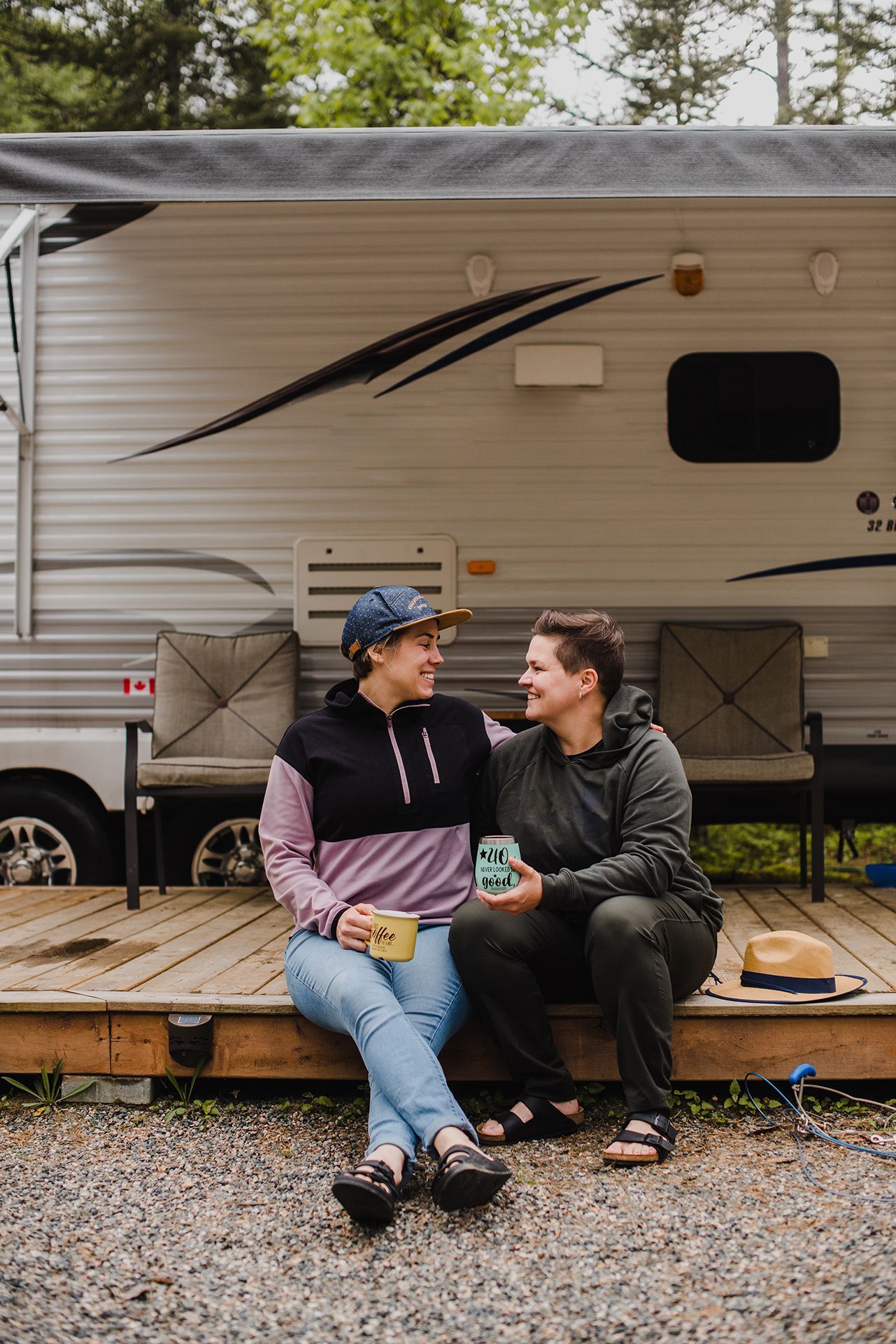 two people sitting on a low wooden deck in front of an rv.