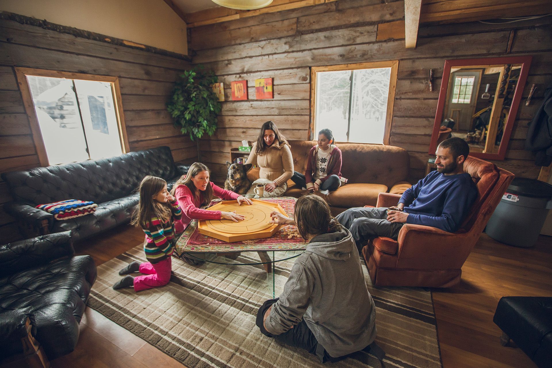 A family sits in the living room of a lodge playing crokinole.