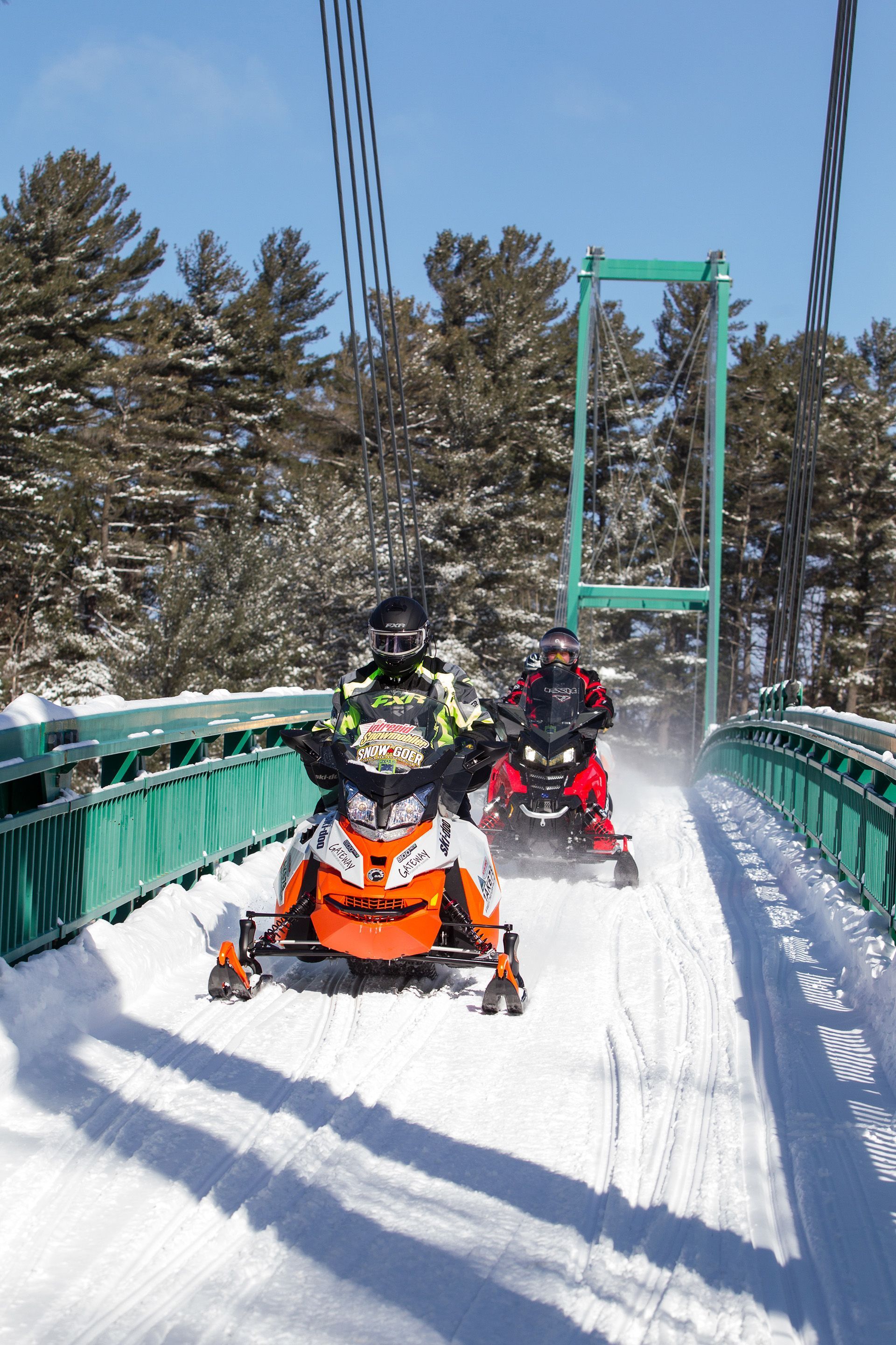 Two people on snowmobiles go over the snowmobile bridge in French River.