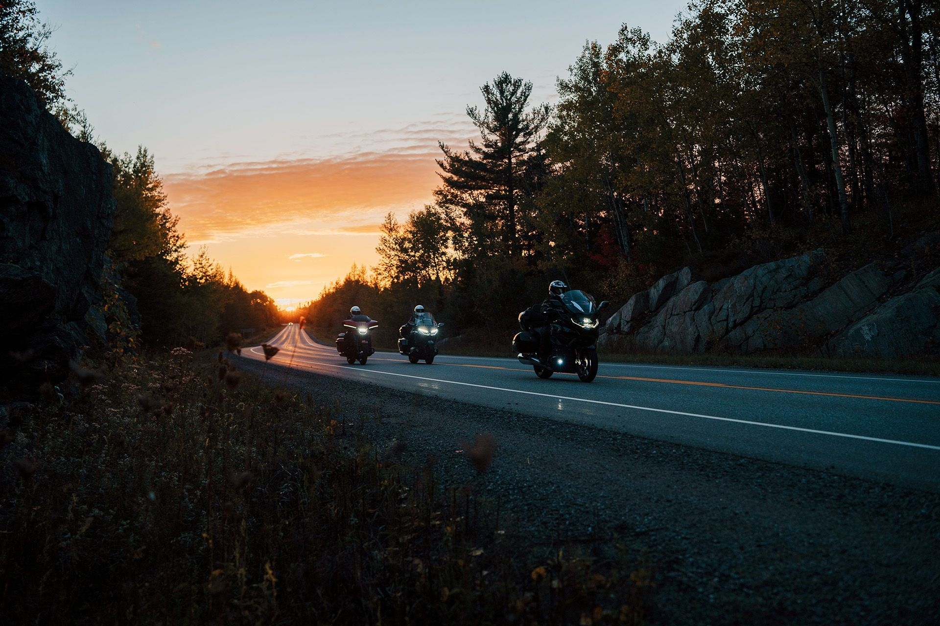 Three motorcyclists drive down a highway at sunset