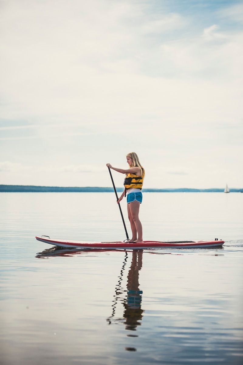 A young woman paddles a stand up paddle board across a serene lake